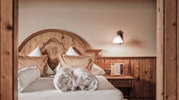 Un letto con struttura in legno, lenzuola bianche e numerosi cuscini, un comodino con una lampada e un pannello di legno a parete.