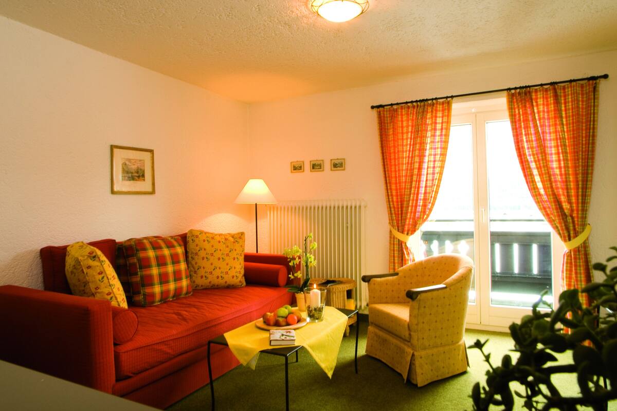 A cozy living room with a red sofa, a yellow table with a fruit bowl, a lamp, and a chair.