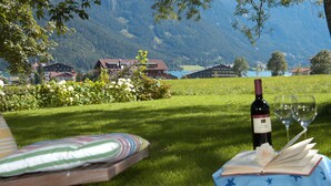A grassy outdoor area with a table set for a meal, a bottle of wine, and a book.