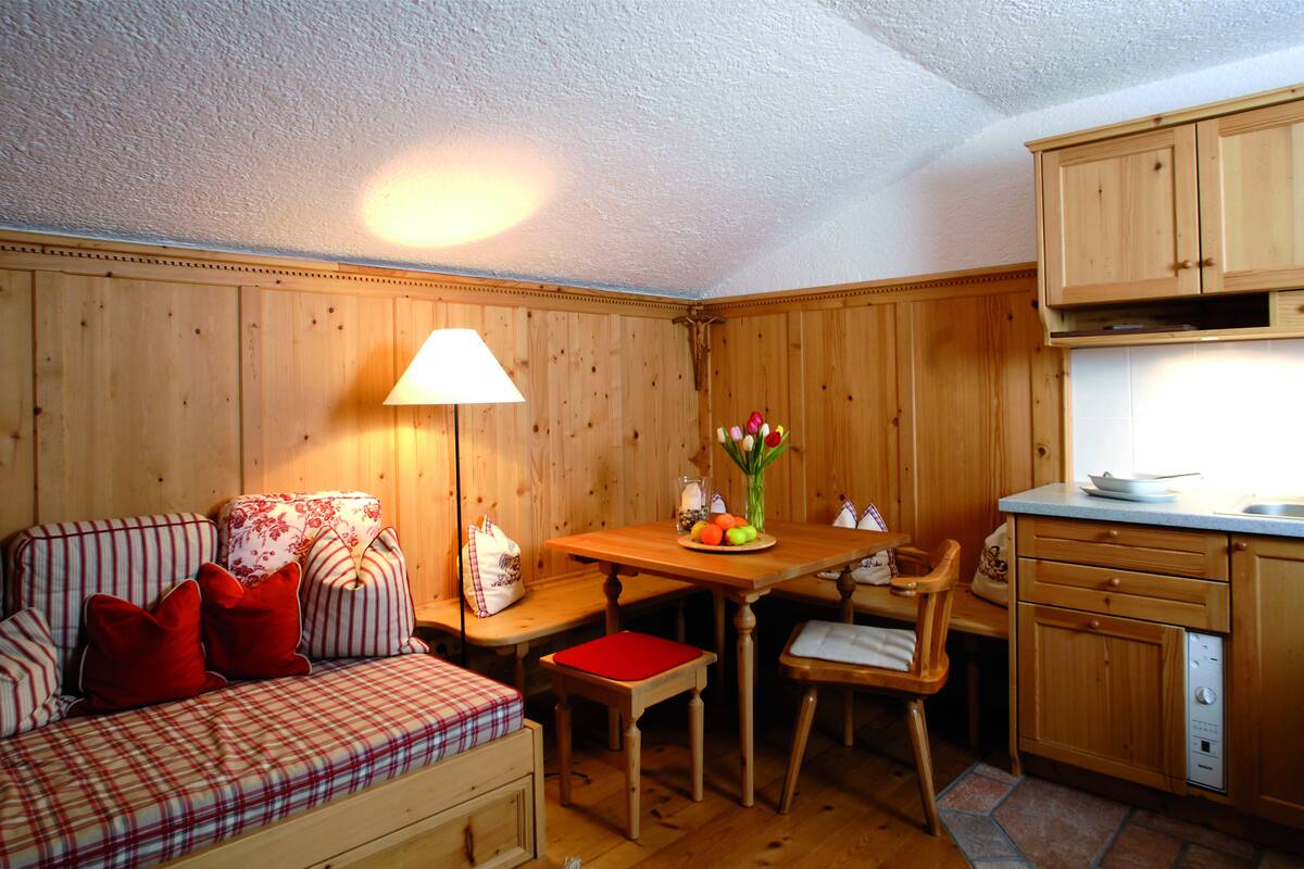 A cozy room with a plaid sofa, a wooden dining table, and a kitchen area with wooden cabinets.