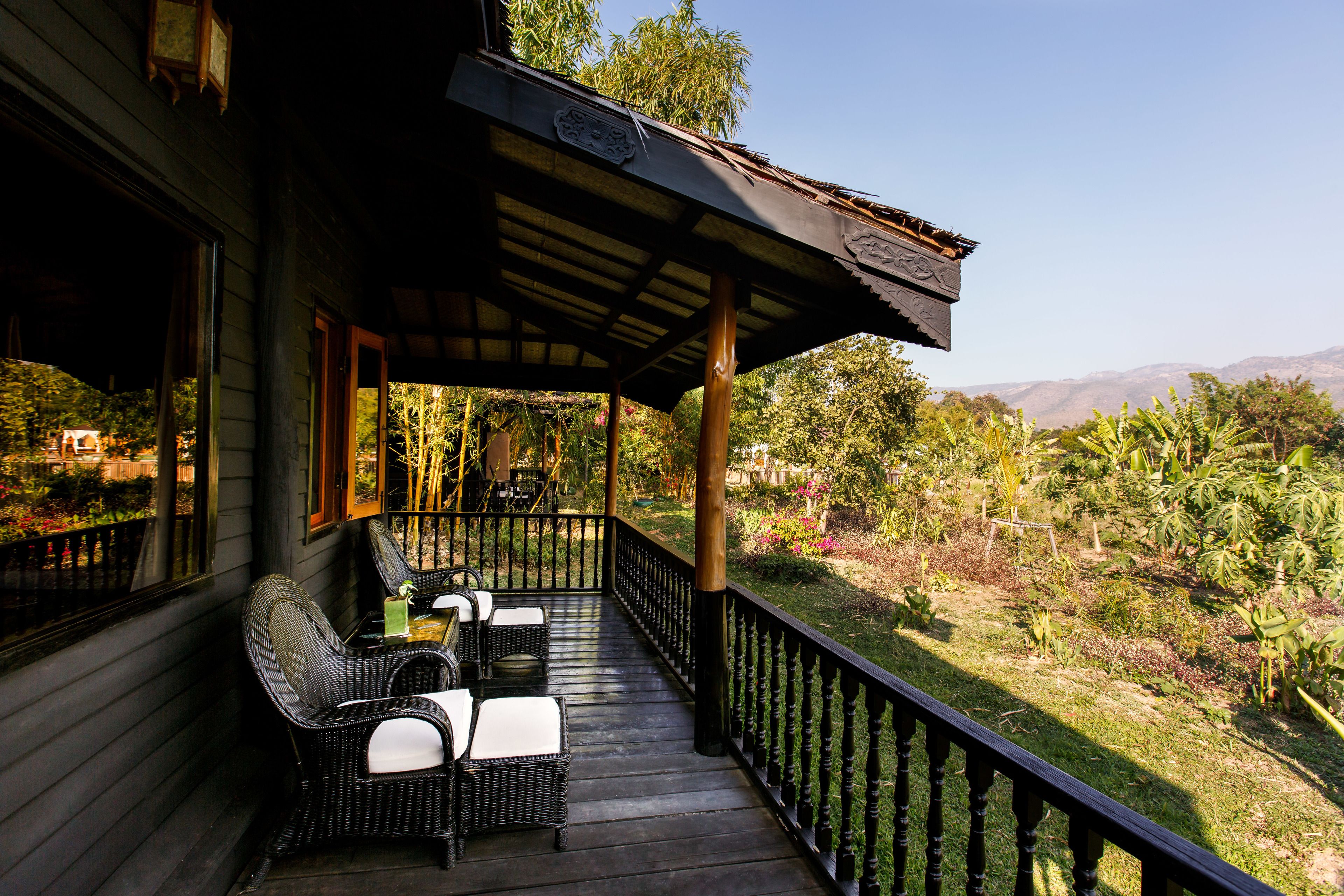 A wooden deck with wicker furniture and a view of a lush garden and distant mountains.