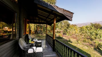 A wooden deck with wicker furniture and a view of a lush garden and distant mountains.