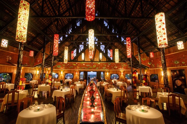 Ein Restaurant mit einem langen Esstisch, mehreren Stühlen und hängenden dekorativen Lampen.