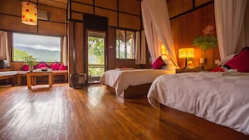 A room with two beds, a wooden floor, a table with chairs, and a view of the outdoors.