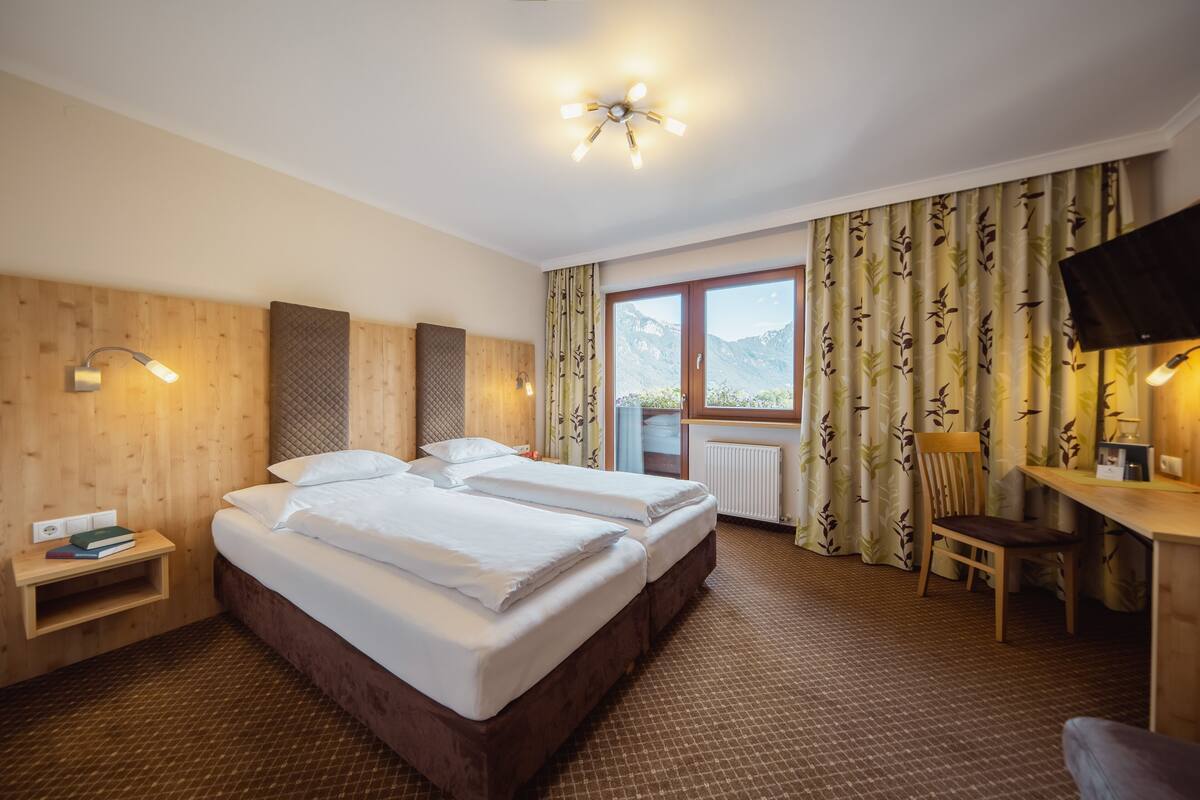 A hotel room with two beds, a desk, a chair, a TV, and a window with curtains.