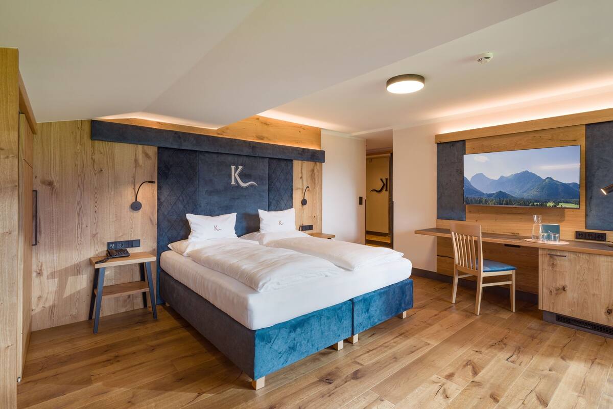 A modern bedroom with a large bed, a desk, and a view of mountains.