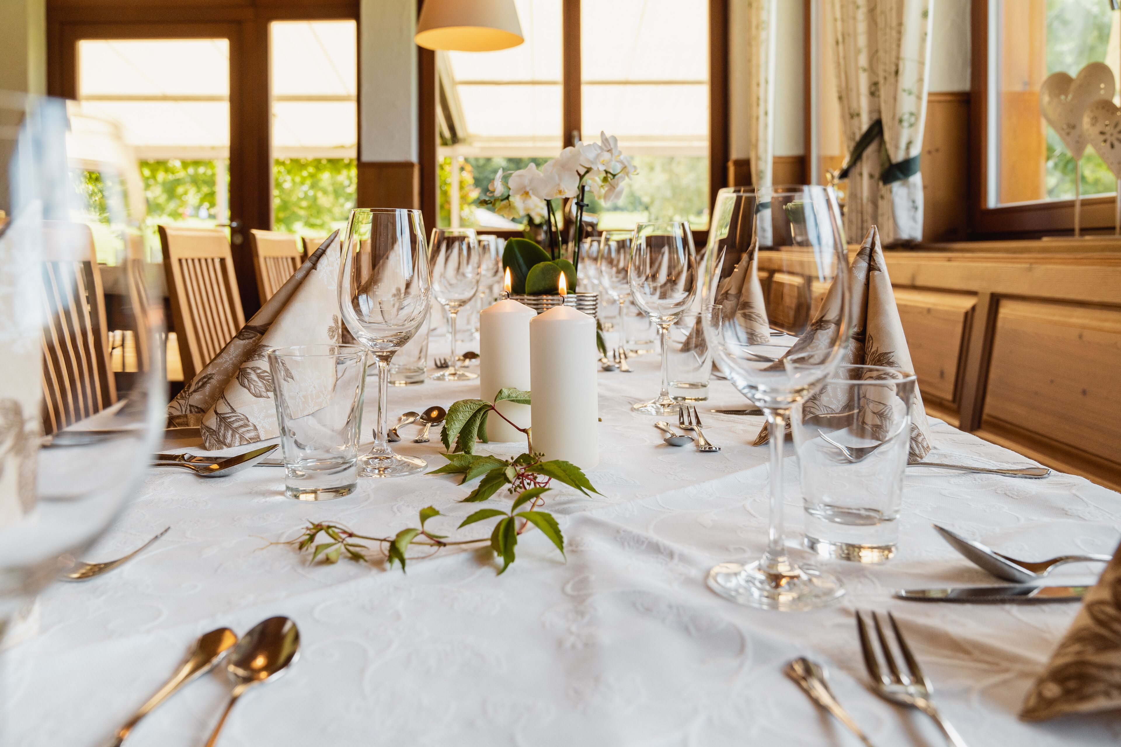 Una mesa de comedor dispuesta con copas de vino, cubiertos y un centro de mesa con vela.