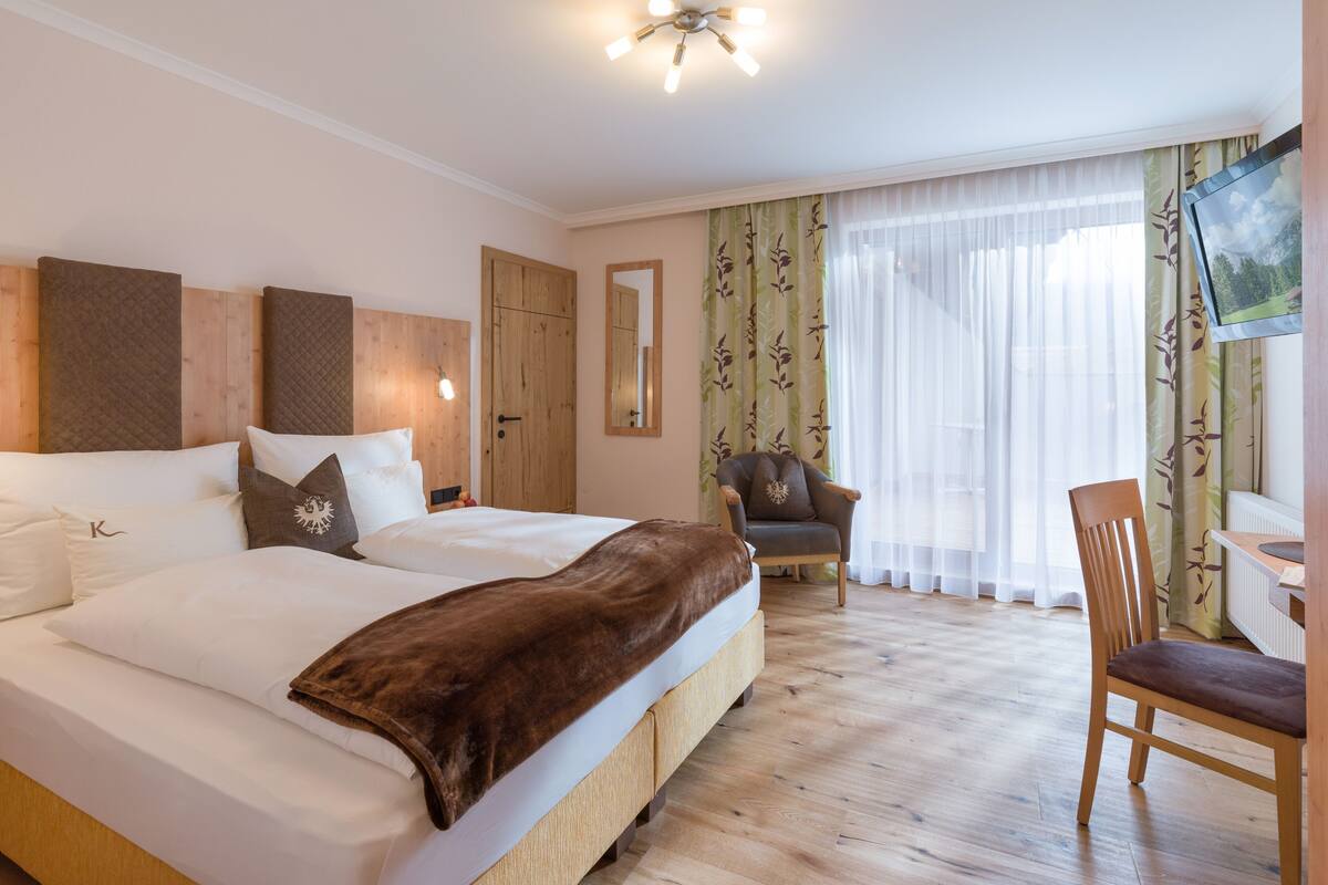 A hotel room with two beds, a wooden headboard, a chair, a desk, and a television.
