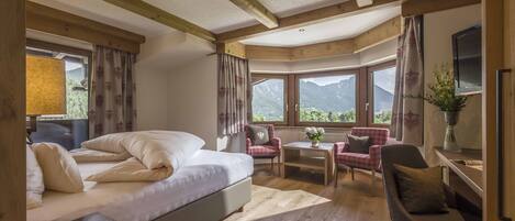 A bedroom with a large bed, a desk, a chair, and a view of mountains through the windows.