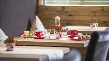 Una mesa de comedor dispuesta con platos rojos y blancos, vasos y una pequeña planta en maceta.