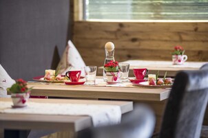 Una mesa de comedor dispuesta con platos rojos y blancos, vasos y una pequeña planta en maceta.