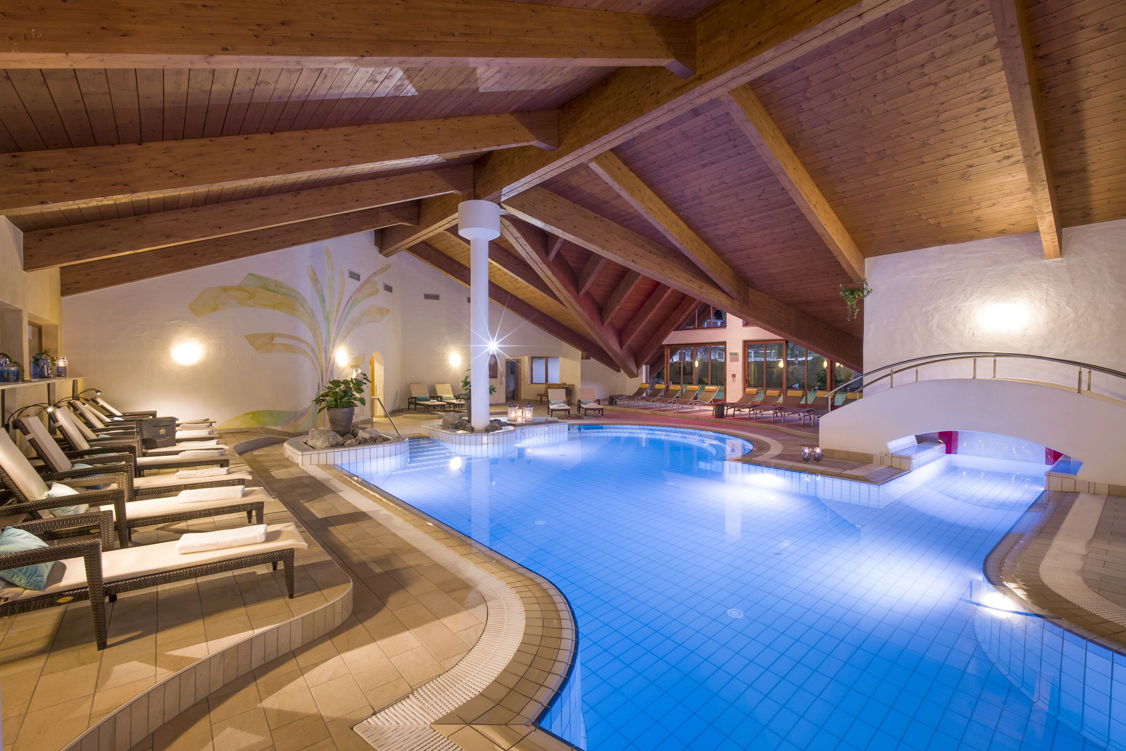 Ein Innenpool mit Holzbalken, Liegestühlen und Fliesenboden.