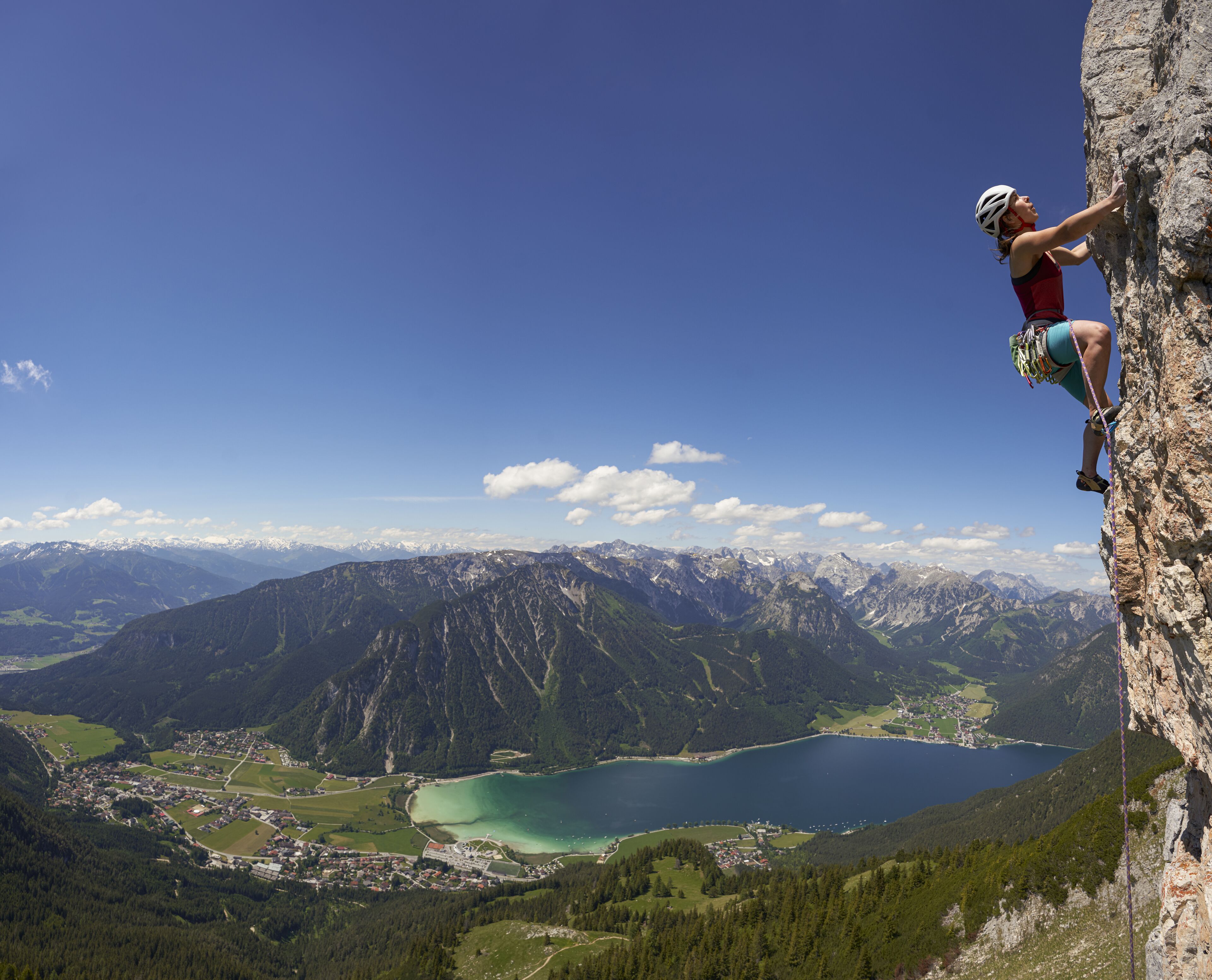 A person rock climbing on a cliff overlooking a lake and mountains.