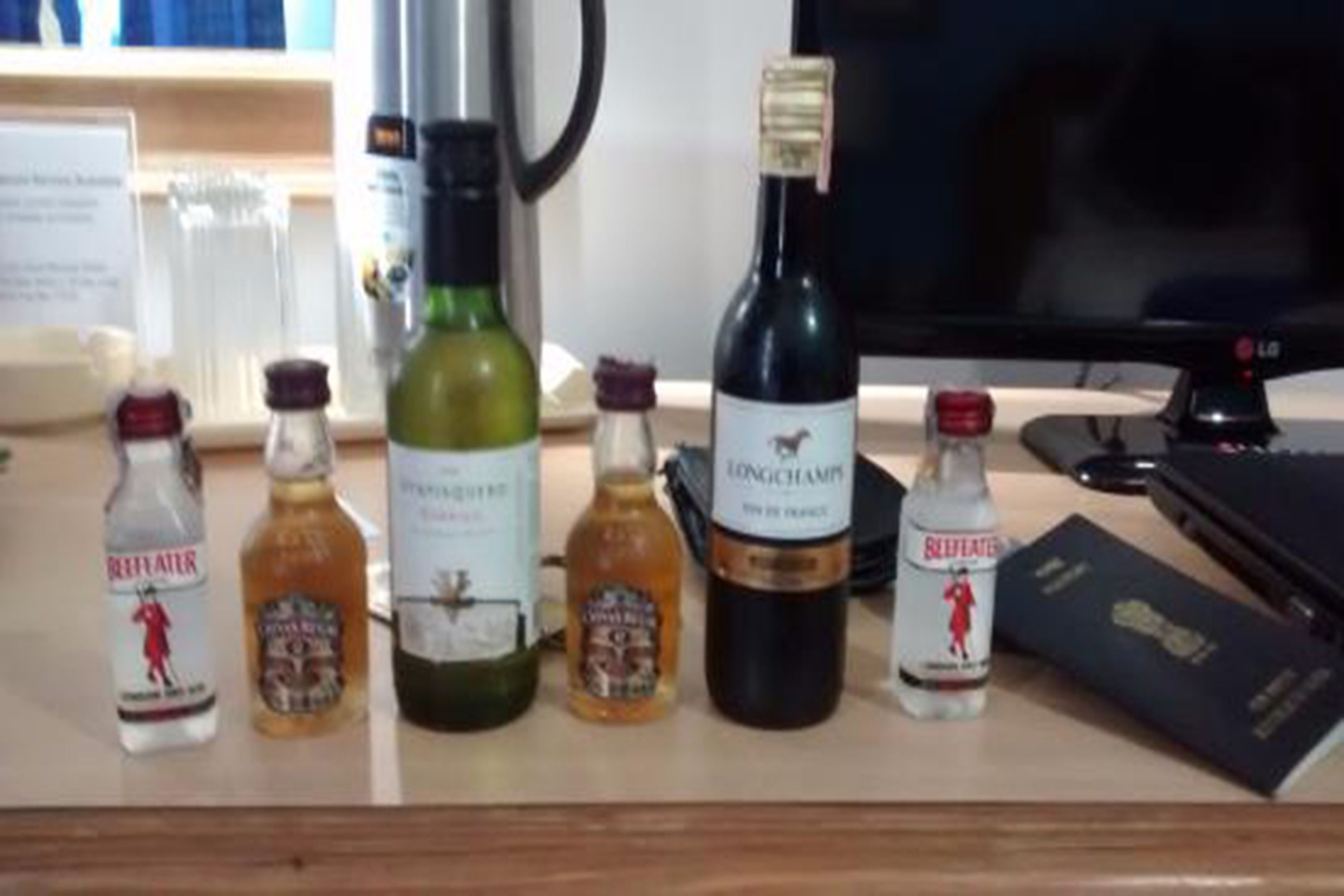 A desk with various bottles of liquor, a computer monitor, and a black folder.