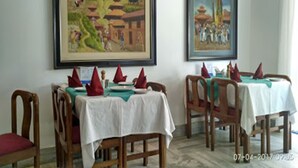 A dining area with tables set for two, wooden chairs, and red napkins. - Hotel Clarion (Lalitpur)