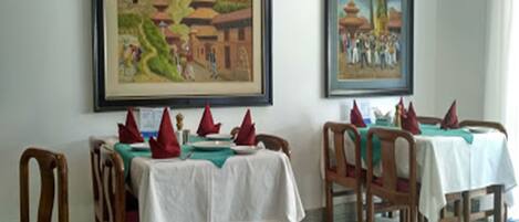 Comedor con mesas dispuestas para dos, sillas de madera y servilletas rojas.
