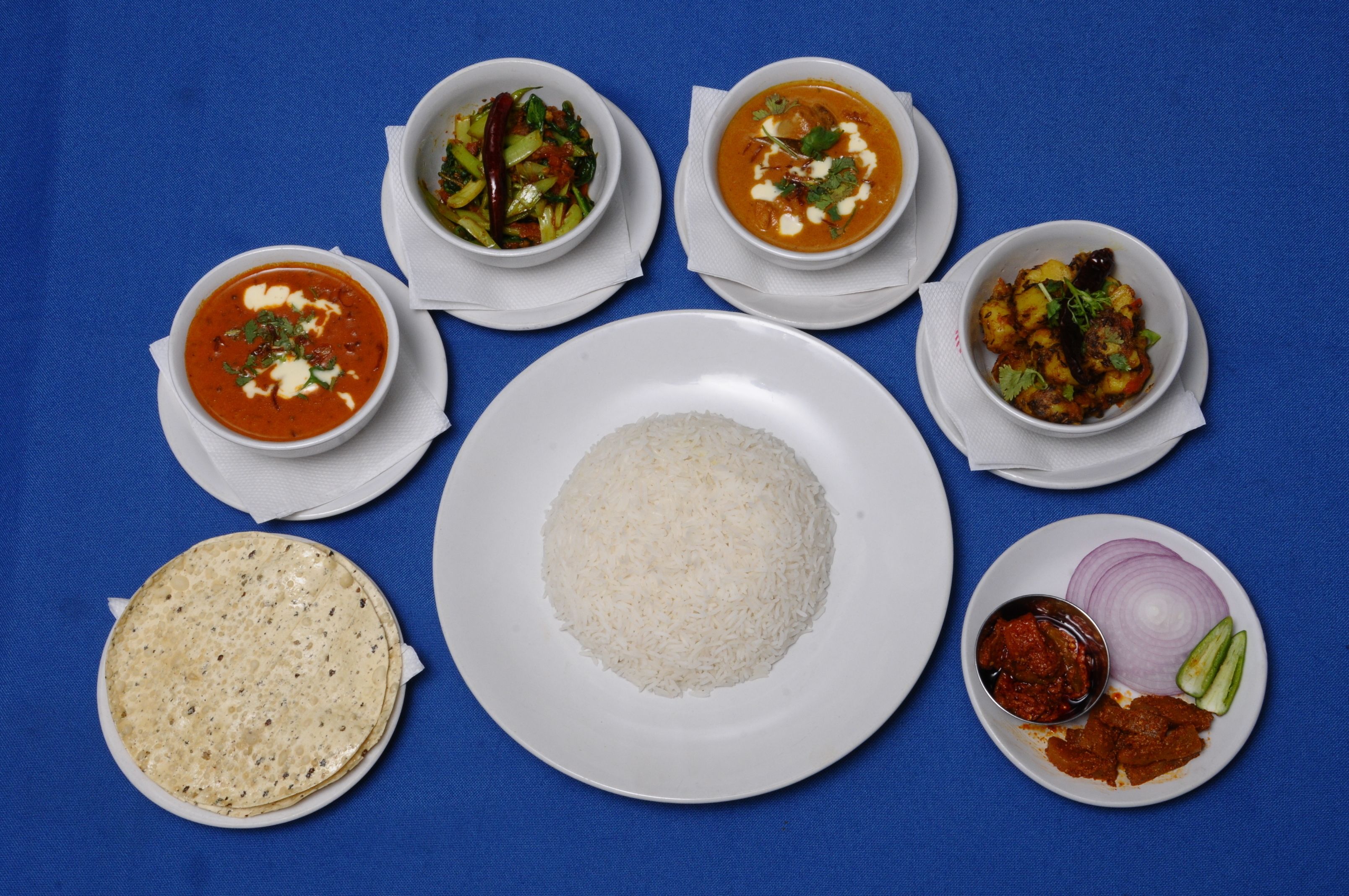 Uma mesa com diversos pratos, incluindo arroz, curry e pão achatado.