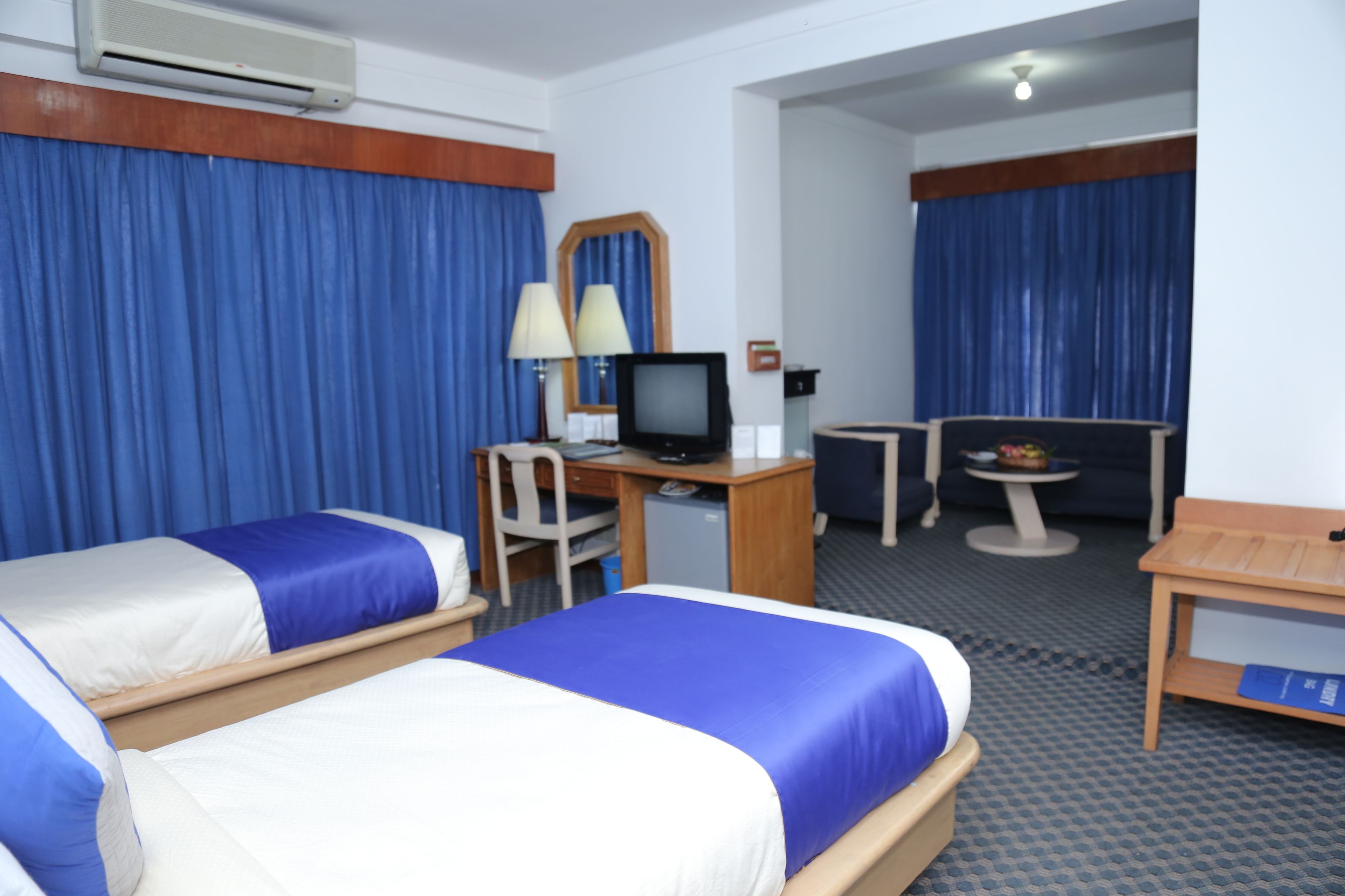 A hotel room with two beds, a desk with a computer, a chair, a small table, and a TV.