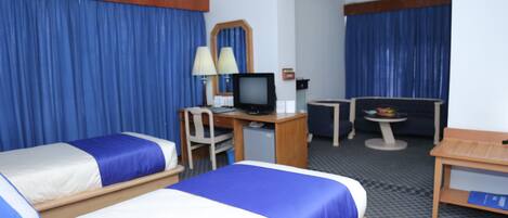 A hotel room with two beds, a desk with a computer, a chair, a small table, and a TV.