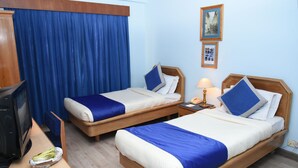 A hotel room with two single beds, a wooden desk with a television, and a blue curtain. - Hotel Clarion (Lalitpur)