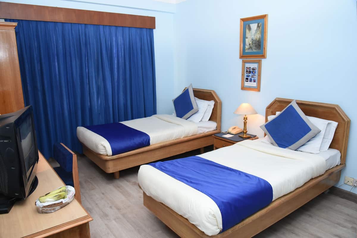 Habitación de hotel con dos camas individuales, un escritorio de madera y un televisor, además de una cortina azul.