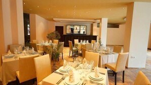 A dining area with multiple tables set for service, a bar in the background, and a neutral color scheme. - St George Palace (ST VLAS)