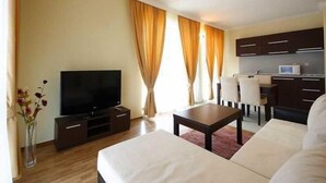 A modern hotel room with a flat-screen TV, a sofa, a coffee table, and a kitchenette. - St George Palace (ST VLAS)