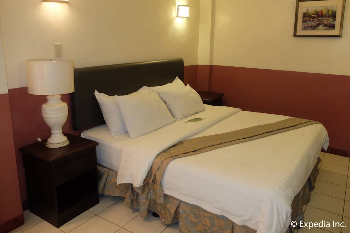A hotel room with a bed, a nightstand, a lamp, and a wall-mounted light fixture.