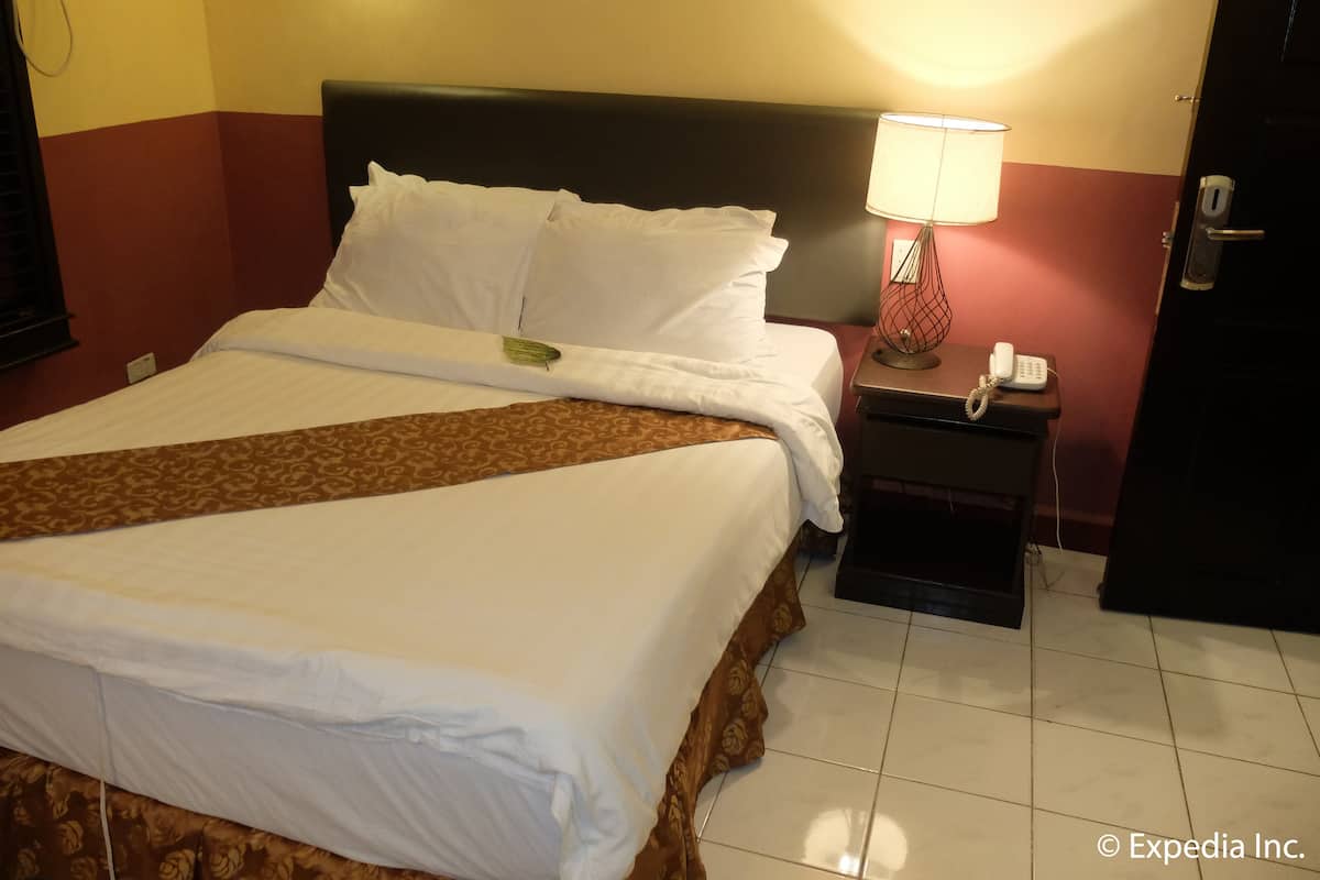 A hotel room with a large bed, a bedside lamp, a telephone, and a door.