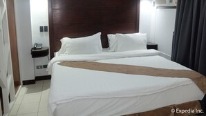 A hotel room with a large bed, a wooden headboard, a bedside table with a phone, and an air conditioning unit. - DM Residente Inns and Villas (Angeles City)