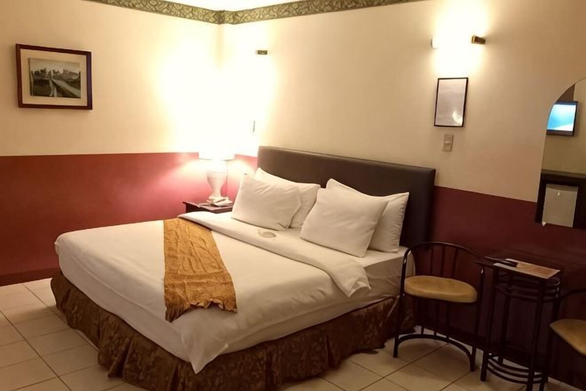 A hotel room with a bed, bedside table, lamp, chair, and a small table.