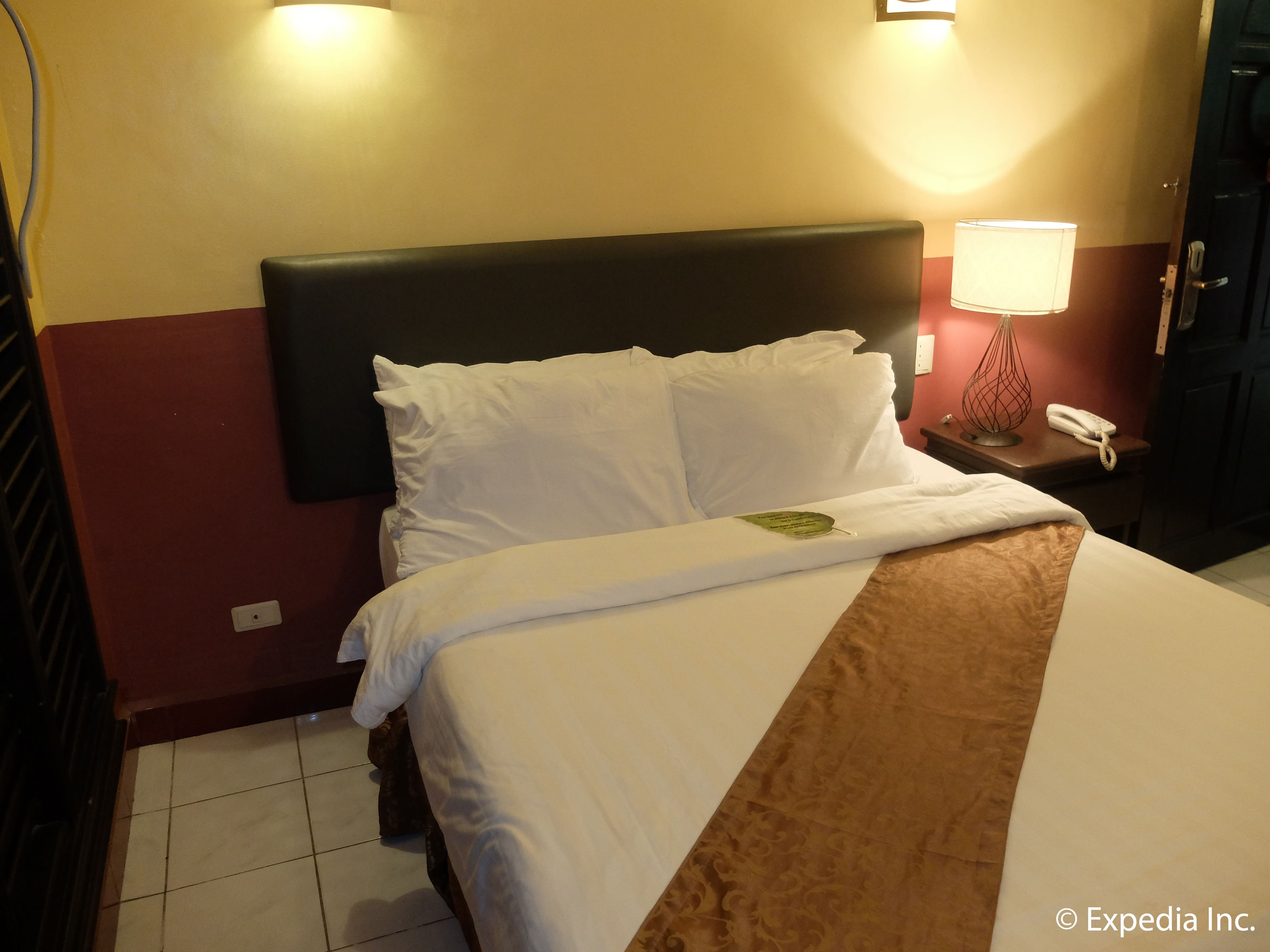 A hotel room with a bed, a nightstand with a lamp, and a telephone.