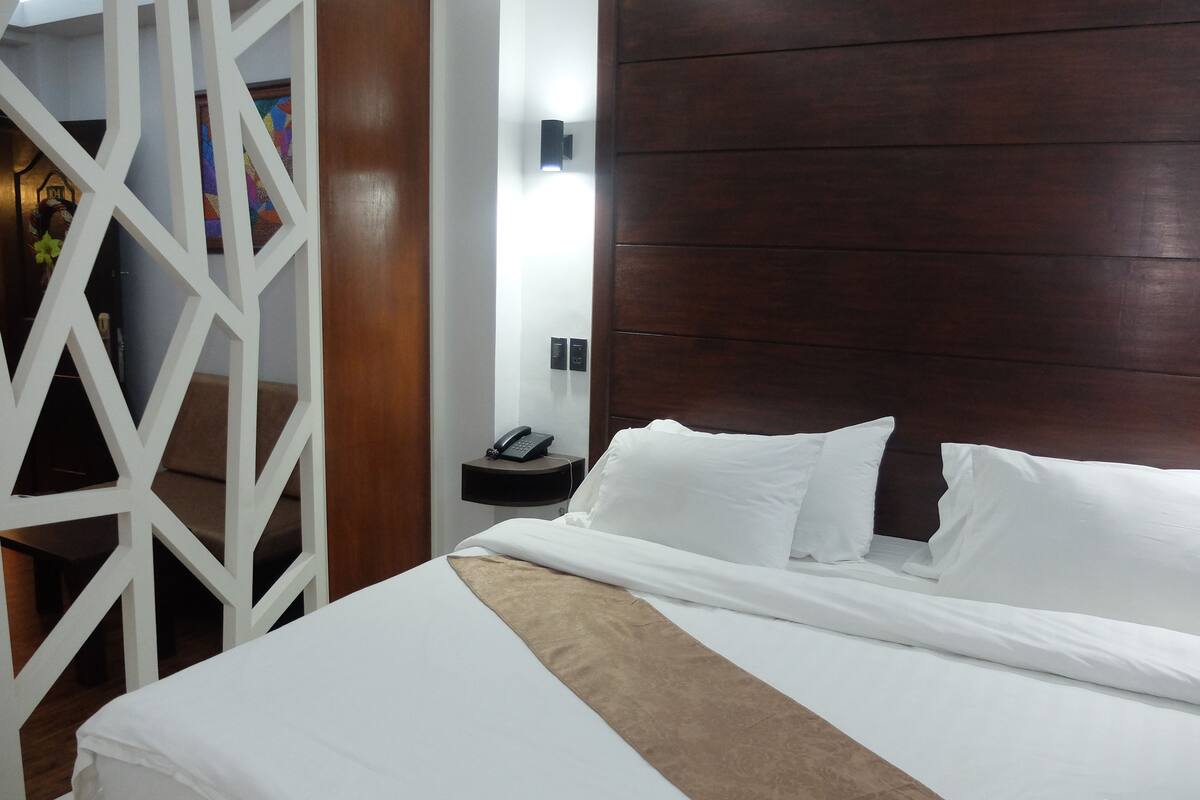 A hotel room with a large bed, a wooden headboard, a bedside phone, and a decorative wall panel.