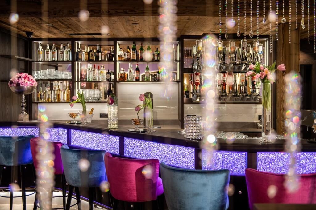 Angolo bar con diverse bottiglie di liquori, un bancone e sedie colorate.