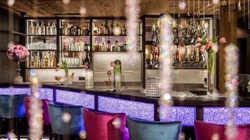 Angolo bar con diverse bottiglie di liquori, un bancone e sedie colorate.