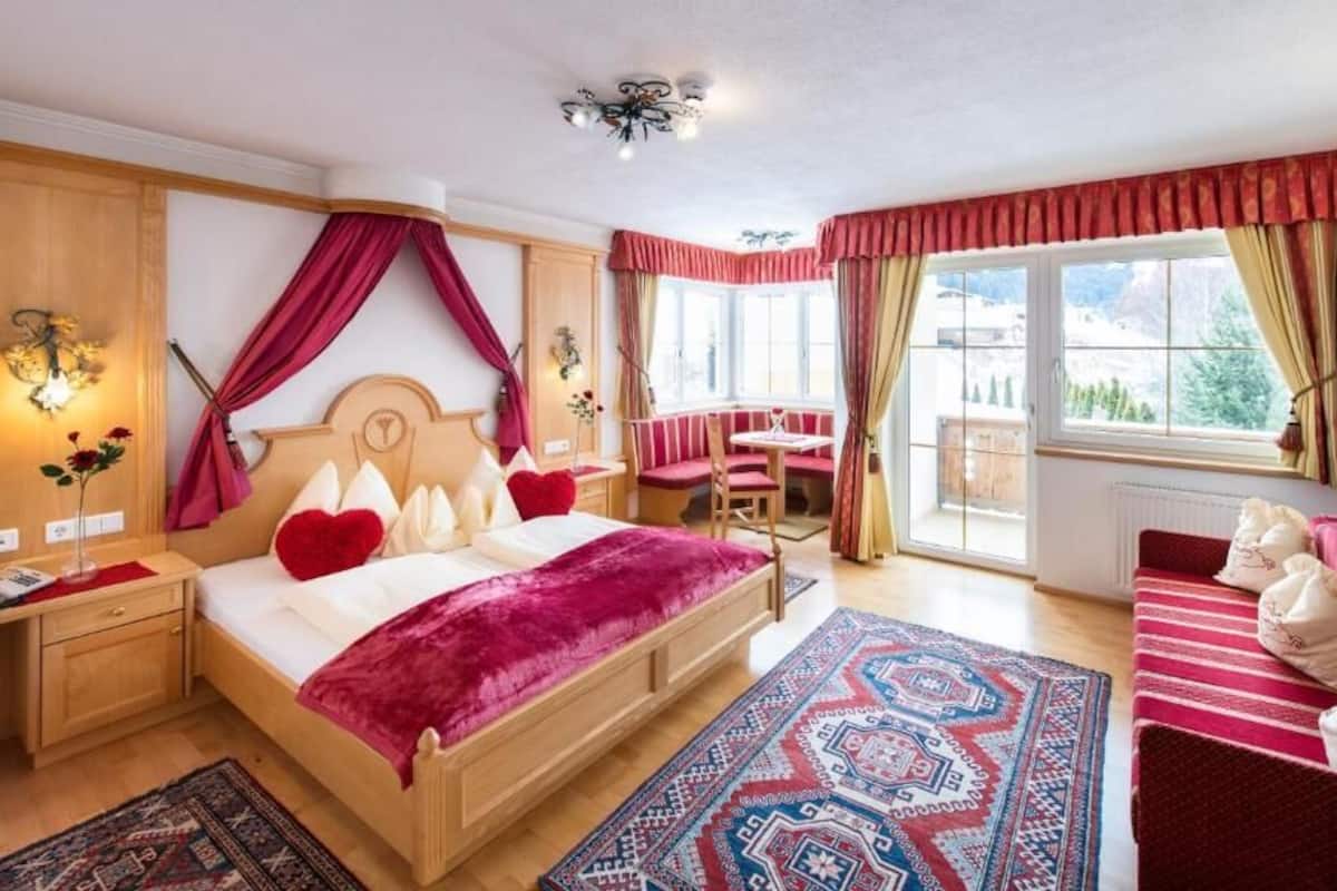 A bedroom with a bed, a desk, a chair, a sofa, and a window with curtains.