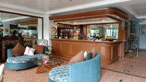 A spacious lobby with a curved wooden reception desk, two blue upholstered sofas with patterned cushions, and a glass coffee table. - Golden Pine Hotel (Baguio)