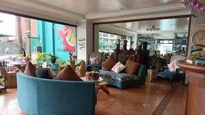 A spacious living area with a large blue sofa, a wooden coffee table, and a variety of decorative items including potted plants and a mirror. - Golden Pine Hotel (Baguio)