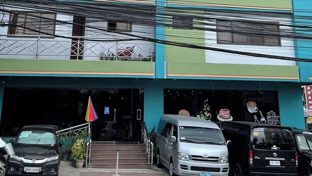 A multi-story building with balconies, a parking area, and a storefront with a sign. - Golden Pine Hotel (Baguio)