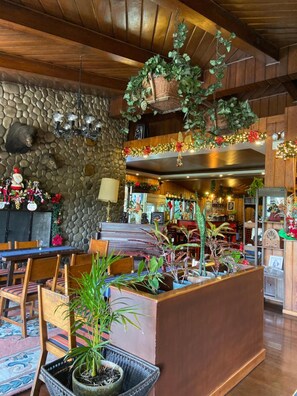 A cozy interior with a stone wall, wooden ceiling, and a central seating area with chairs and tables. - Mountain Lodge (Baguio)