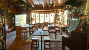 A cozy restaurant interior with wooden tables and chairs, a Christmas tree, and a stone wall. - Mountain Lodge (Baguio)