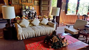 A cozy living room with a sofa, a coffee table with a floral centerpiece, and a chair. There are lamps on either side of the sofa and a wooden door in the background. - Mountain Lodge (Baguio)