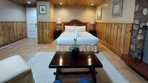 A hotel room with a wooden ceiling, a bed with white linens, two bedside tables with lamps, a small table with a plant, and a stone wall. - Mountain Lodge (Baguio)