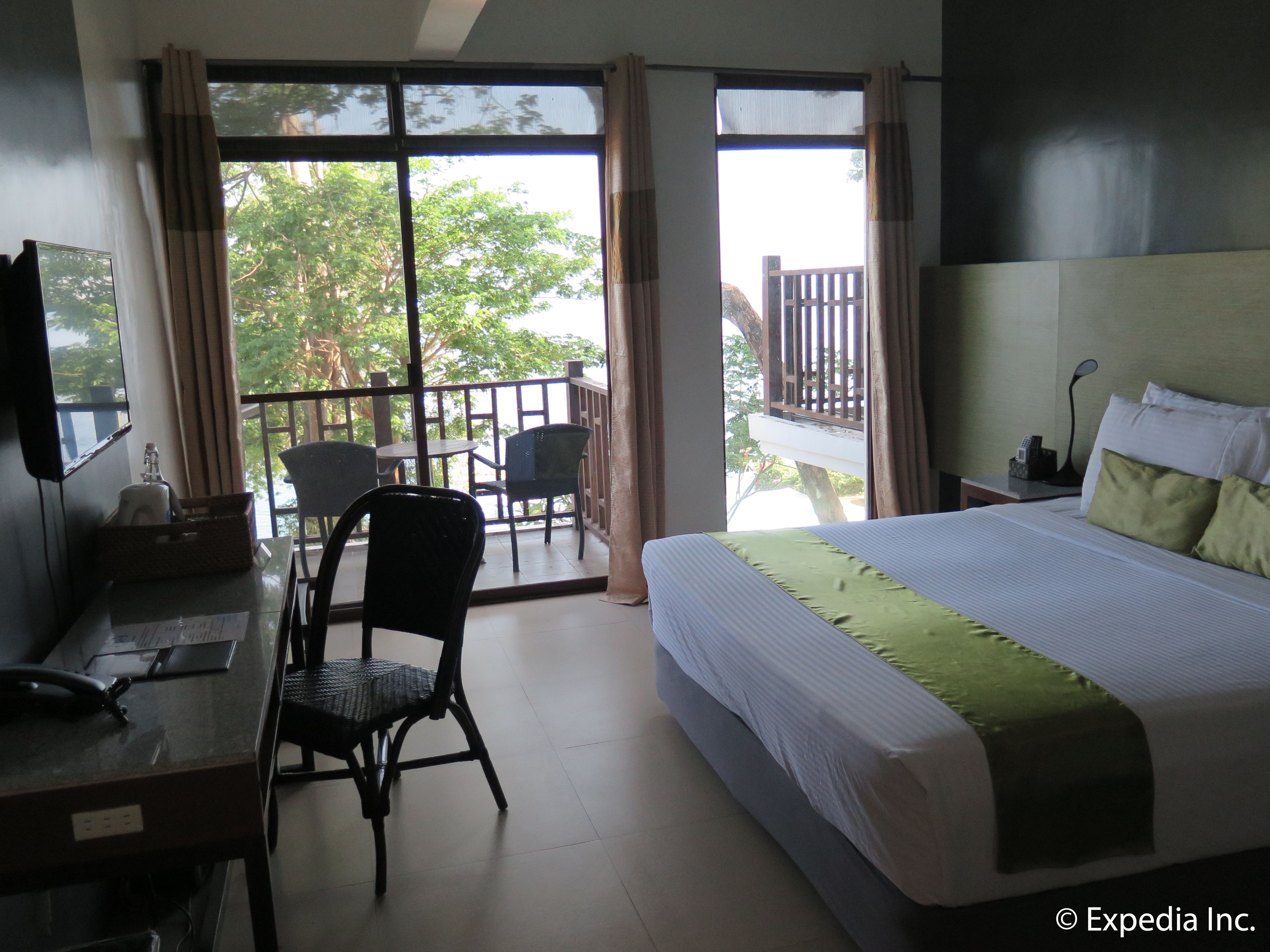 Habitación de hotel con cama, escritorio, silla y balcón con vista a árboles.