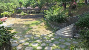 A garden with stone pathways, thatched-roof structures, and a stone staircase. - Aiyanar Beach and Dive Resort (Mabini)