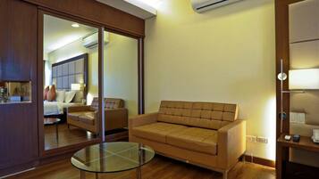 Una sala moderna con una mesa de centro de vidrio, un sofá y una puerta corredera con espejo que da a un dormitorio.