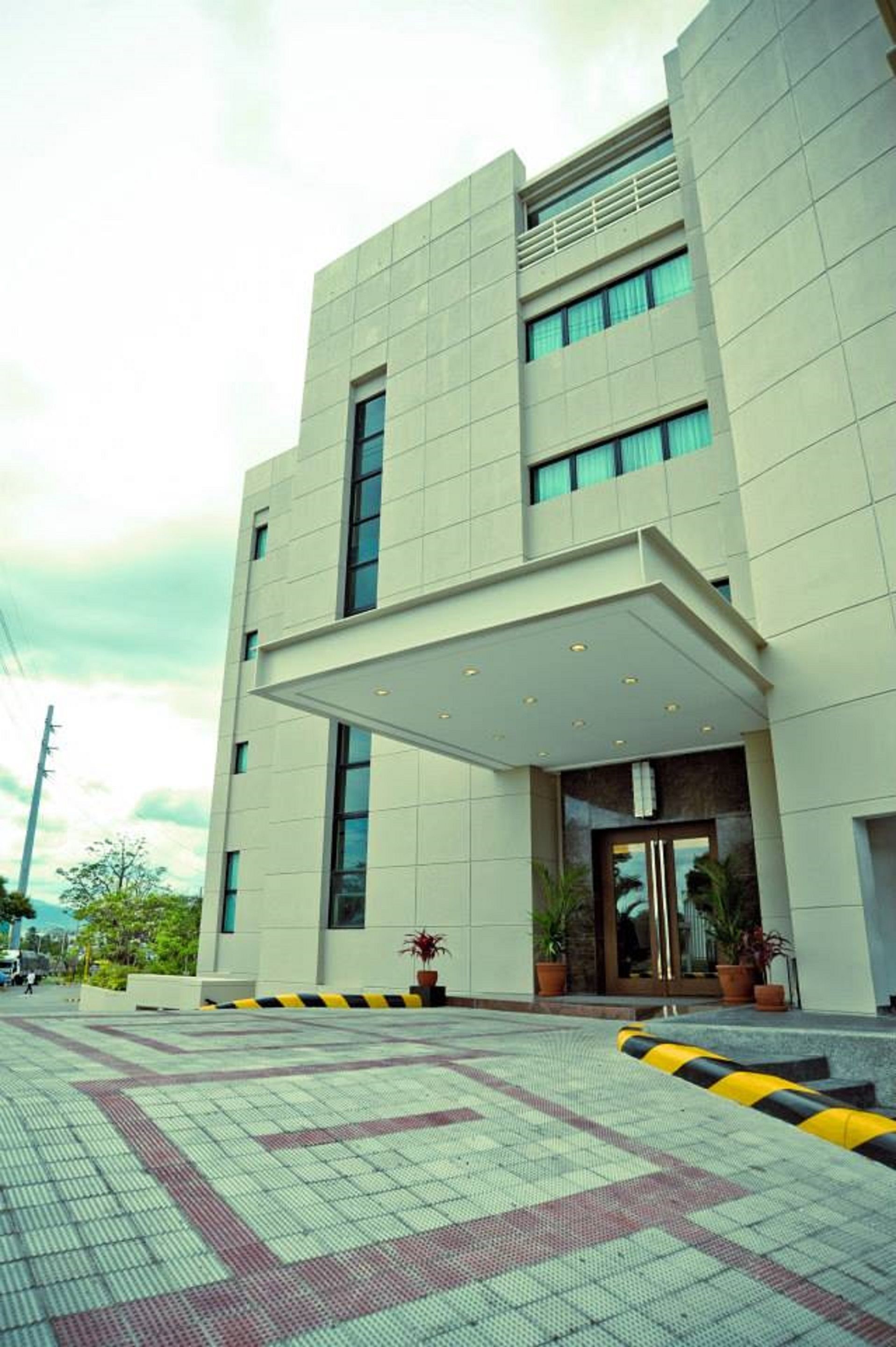 A modern building with a flat facade, large windows, and a covered entrance area with potted plants.