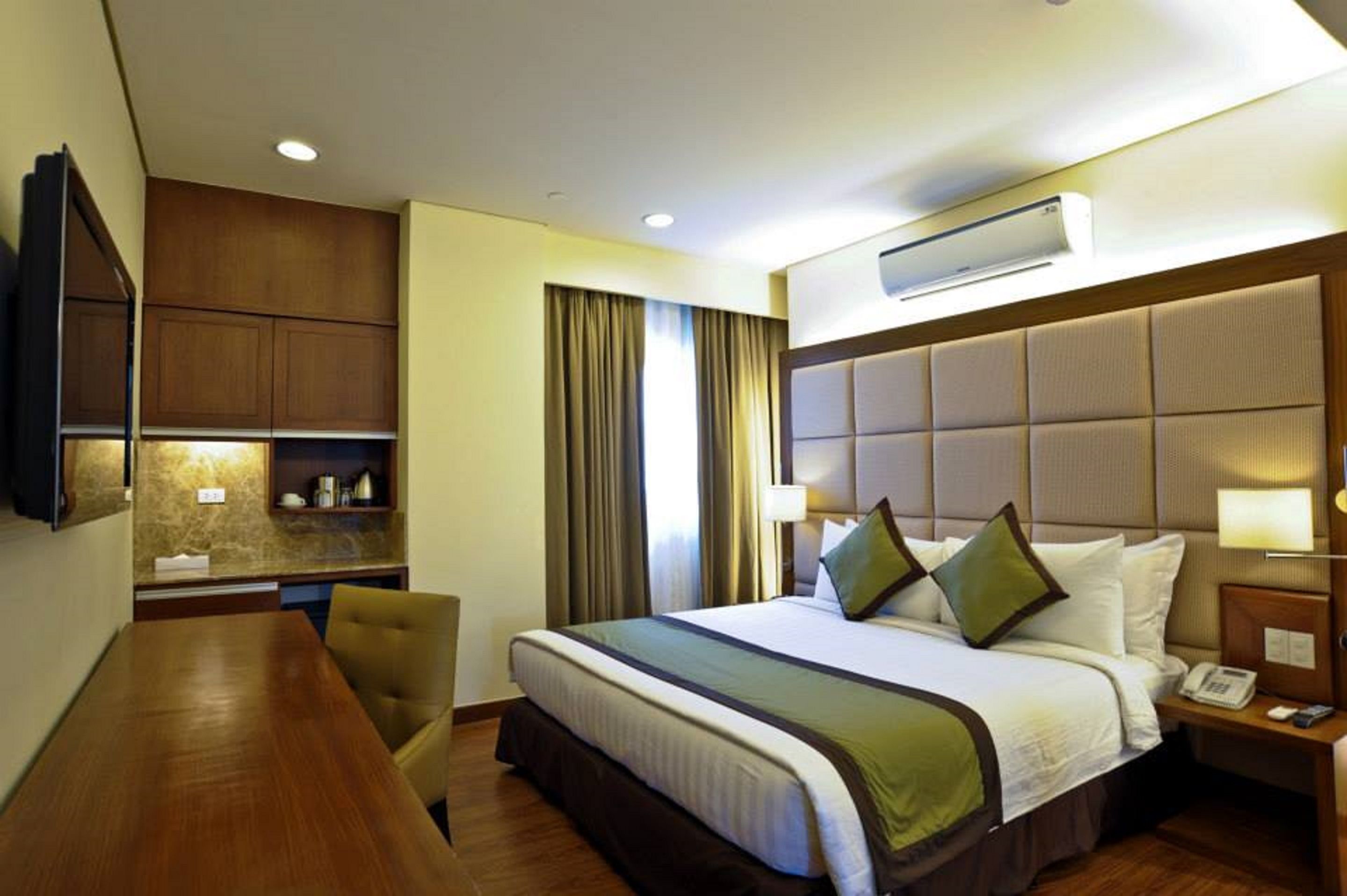 A hotel room with a bed, bedside table, lamp, and a TV mounted on the wall.