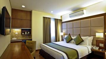 A hotel room with a bed, bedside table, lamp, and a TV mounted on the wall.