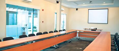 A conference room with a long table, chairs, a projector screen, and large windows.